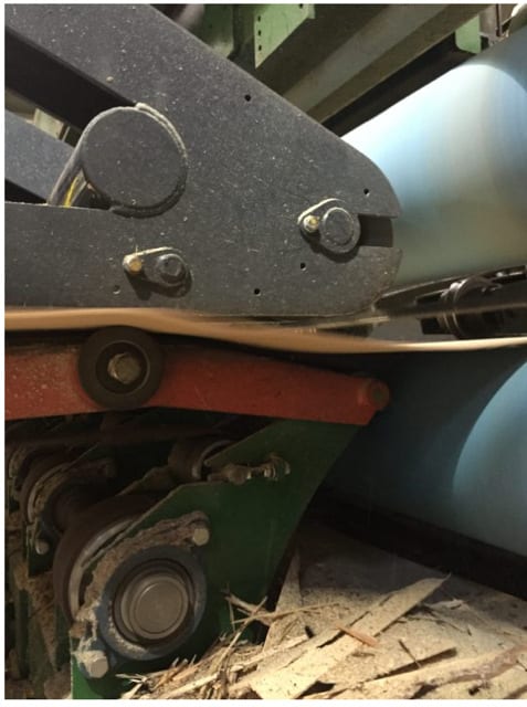 Close-up of industrial wood processing machinery with rollers, gears, and sawdust below.