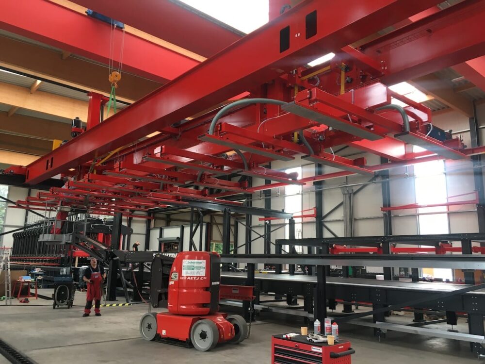 Large red industrial machinery and overhead cranes operate inside a spacious factory producing Mass Ply Panels.
