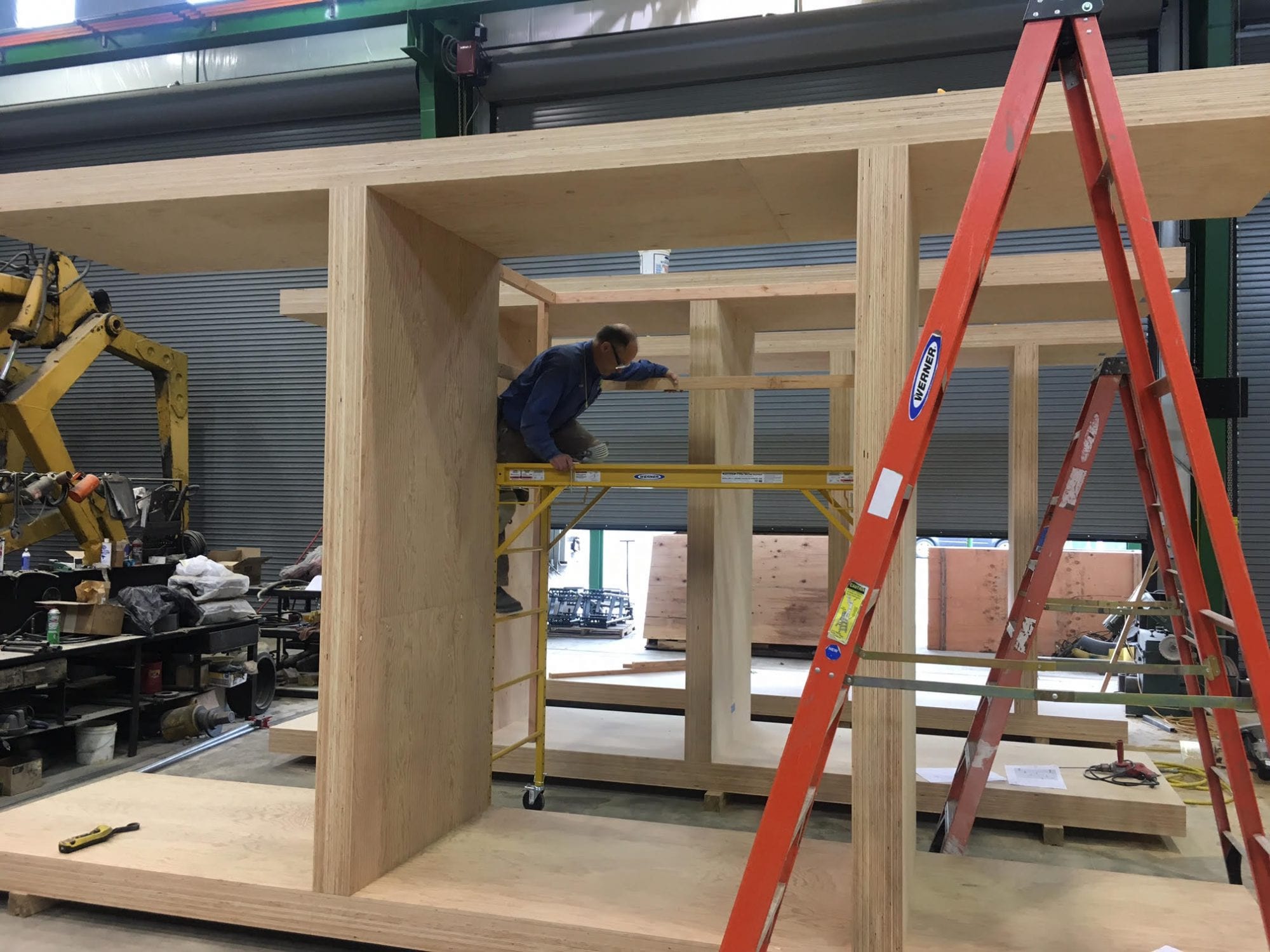 Person building a large wooden structure indoors, standing on scaffolding beside a red ladder—a testament to craftsmanship and the growing .