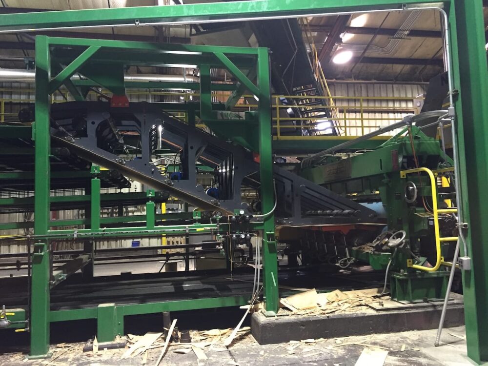 Large green industrial wood processing machine inside a factory, with wood pieces on the floor.