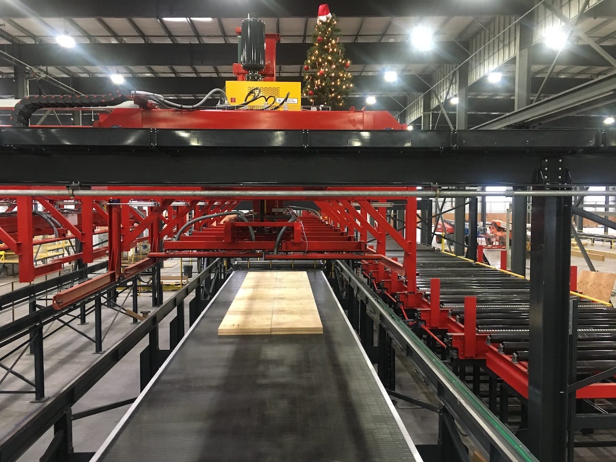 A factory conveyor system with a Mass Ply Panel sheet of wood and a decorated Christmas tree on top of a machine.