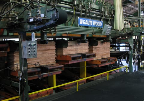 Stacks of thin wood sheets in a large industrial machine at a wood processing facility.