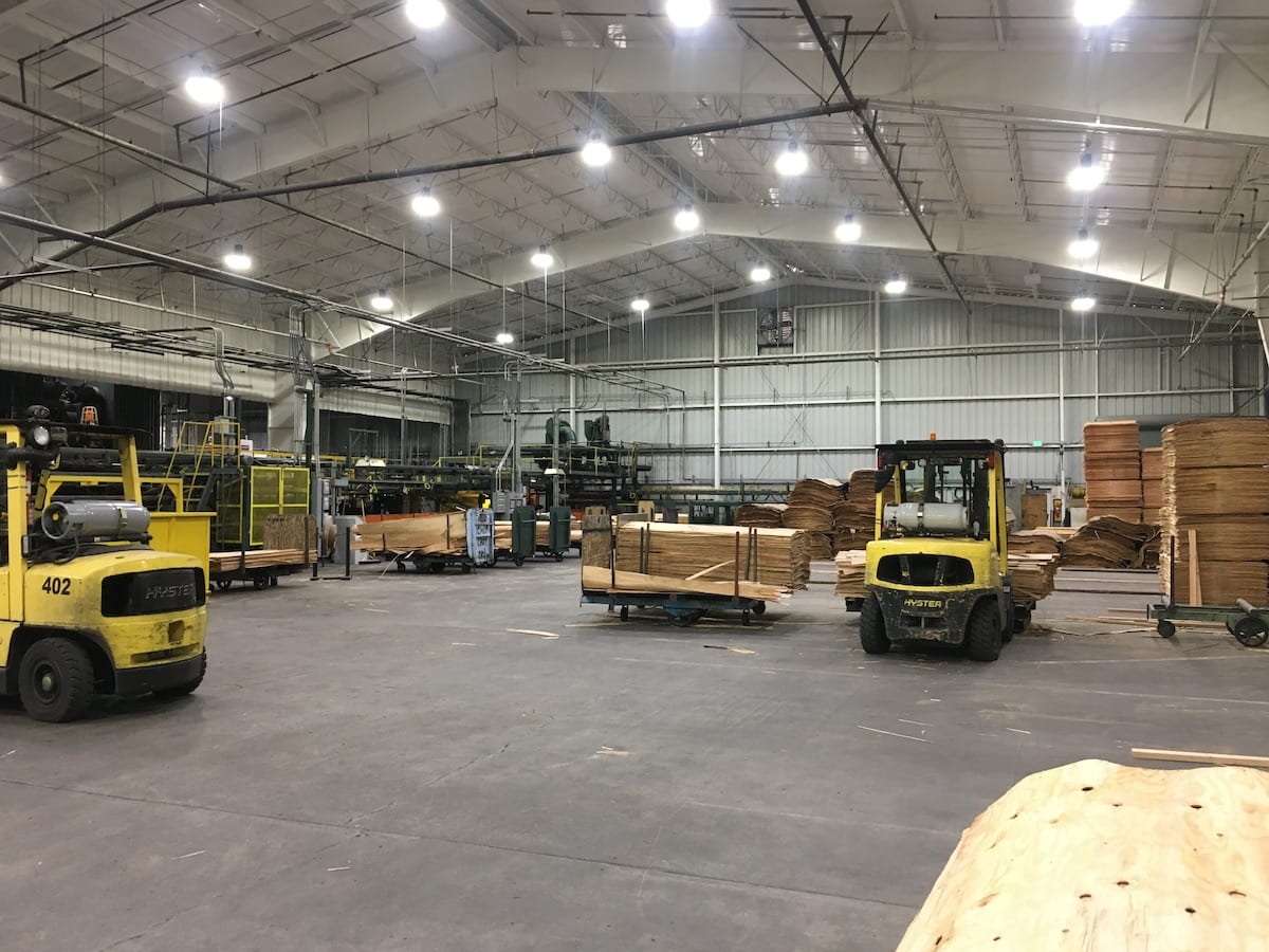 Large warehouse with forklifts, stacks of plywood, and overhead lights in a spacious industrial setting—perfect for winter trading in commodities.