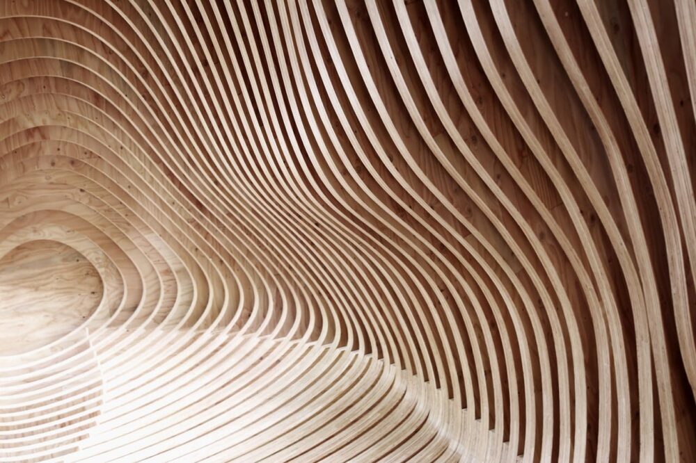 Curved wooden slats create an abstract, flowing wave pattern against a wall and floor.