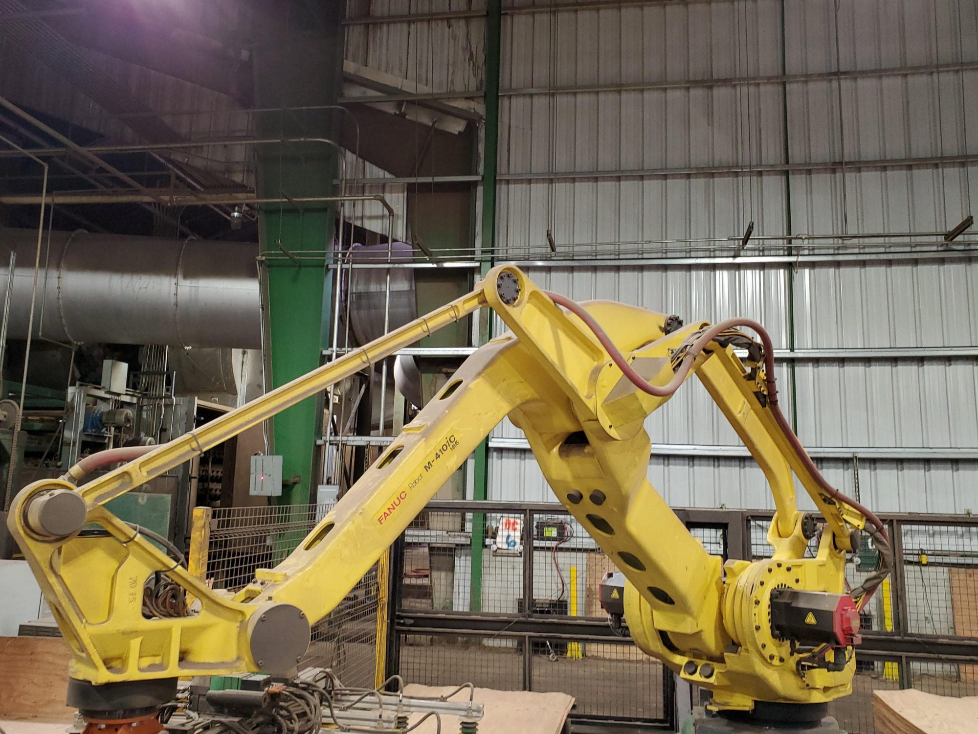 A large yellow industrial robot arm, exemplifying the power of robots versus machines, is positioned inside a metal-walled factory or warehouse.