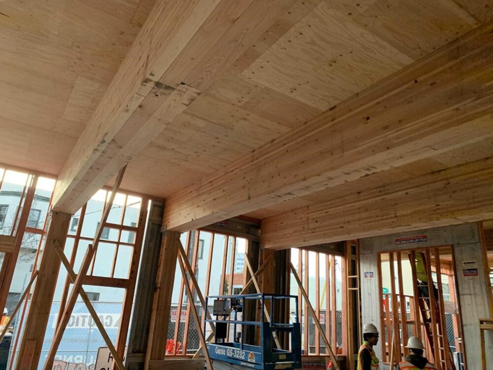 Wood framing and beams in a building under construction, with workers and equipment visible below.