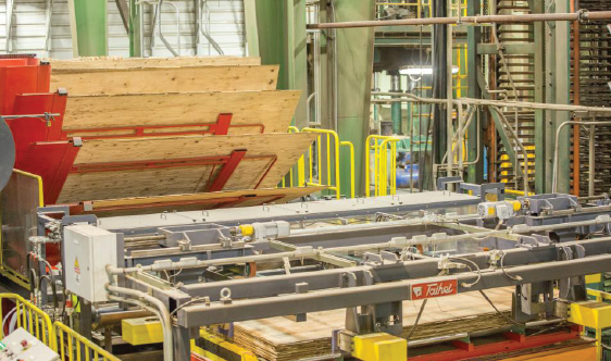 Sheets of plywood are stacked and processed by machinery in an industrial wood manufacturing facility.