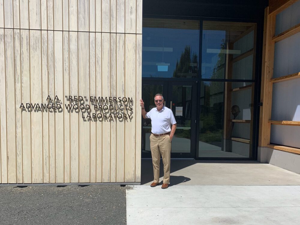A man in a white shirt stands in front of the Advanced Wood Products Laboratory building entrance near the new OSU Peavy Hall.