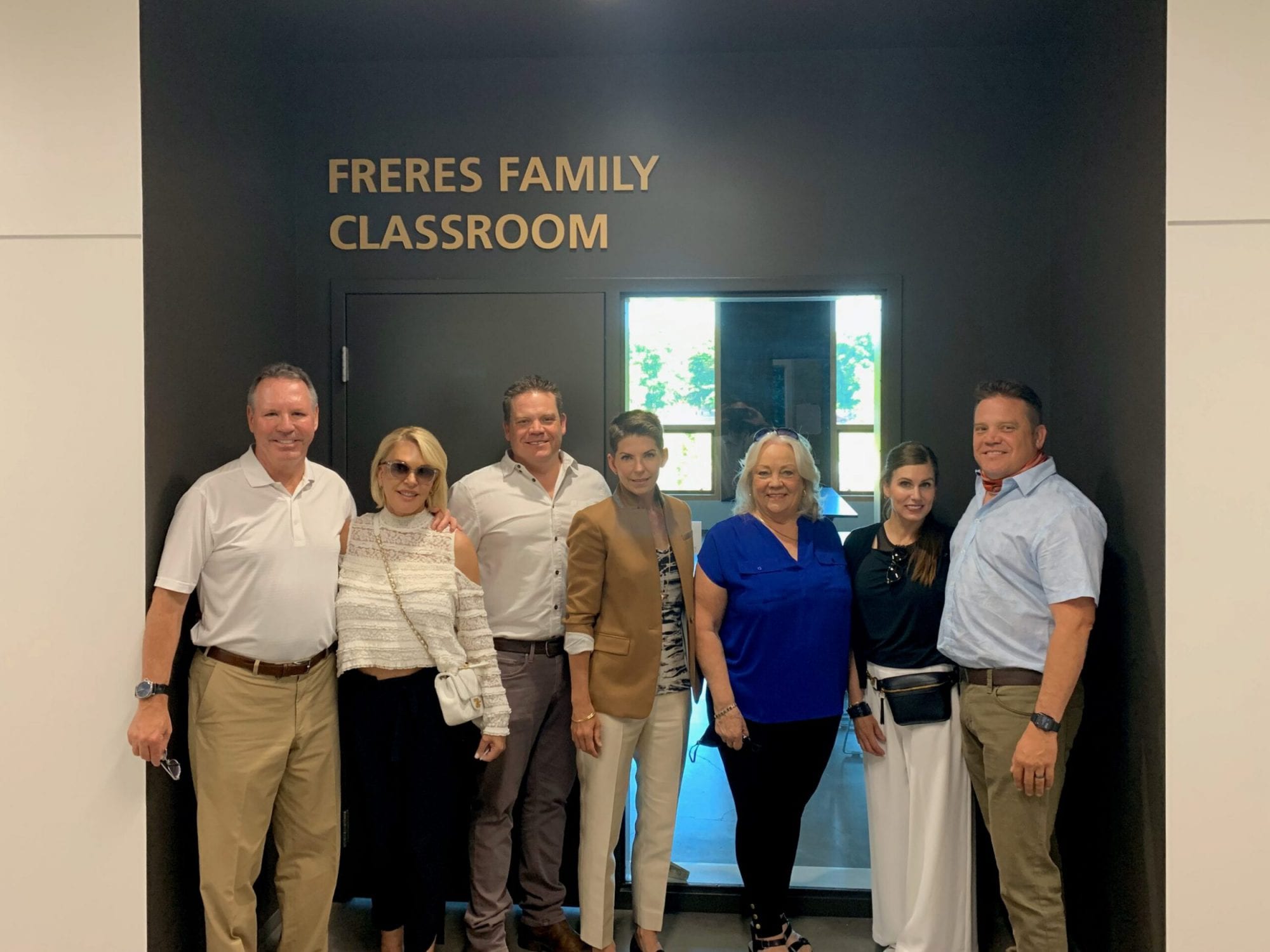 Seven people stand smiling in front of a door labeled Freres Family Classroom in the new OSU Peavy Hall.