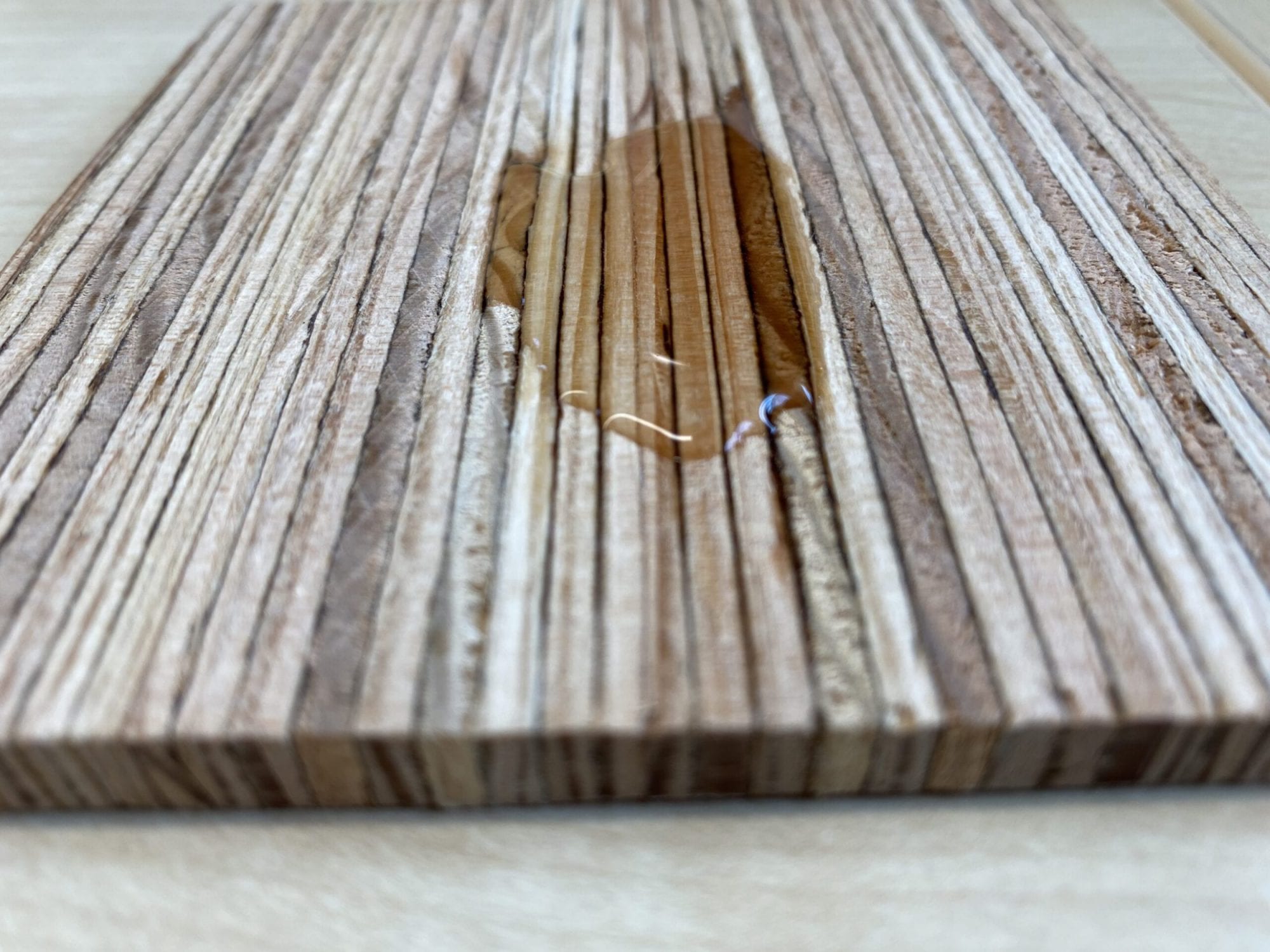 A close-up of a wooden plank with a small puddle of liquid on its grooved surface.