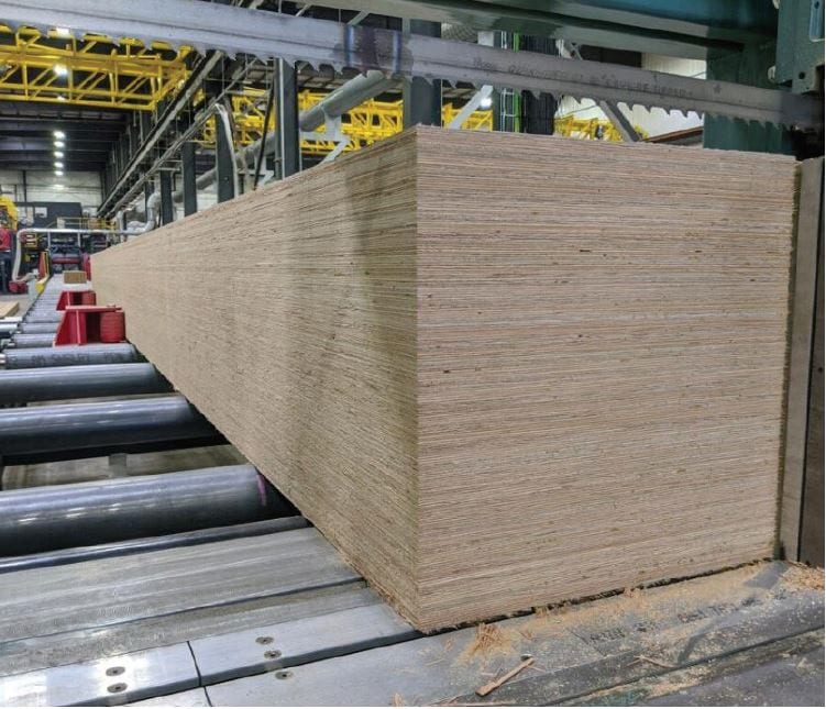 Large stack of plywood sheets on rollers in a factory setting.