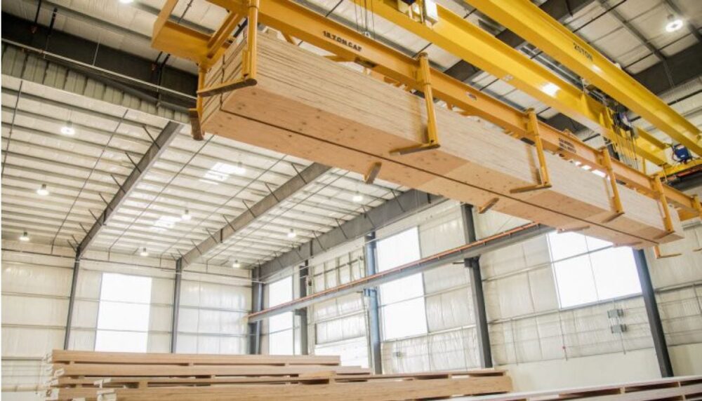 A crane lifts large wooden panels inside a spacious, well-lit industrial warehouse.