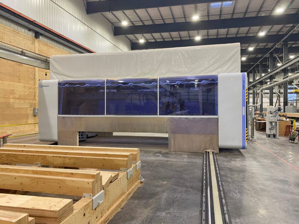 Large industrial CNC Nesting machine in a factory, with wood beams and high ceilings visible in the background.