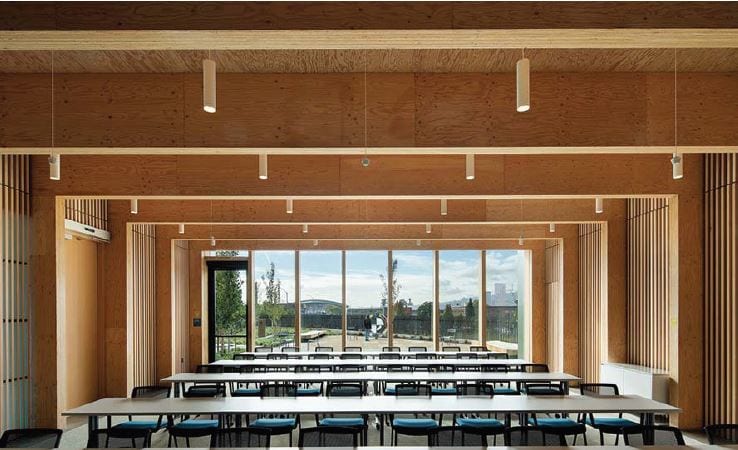 A modern, wooden classroom with rows of tables and chairs facing large windows with a view outside.