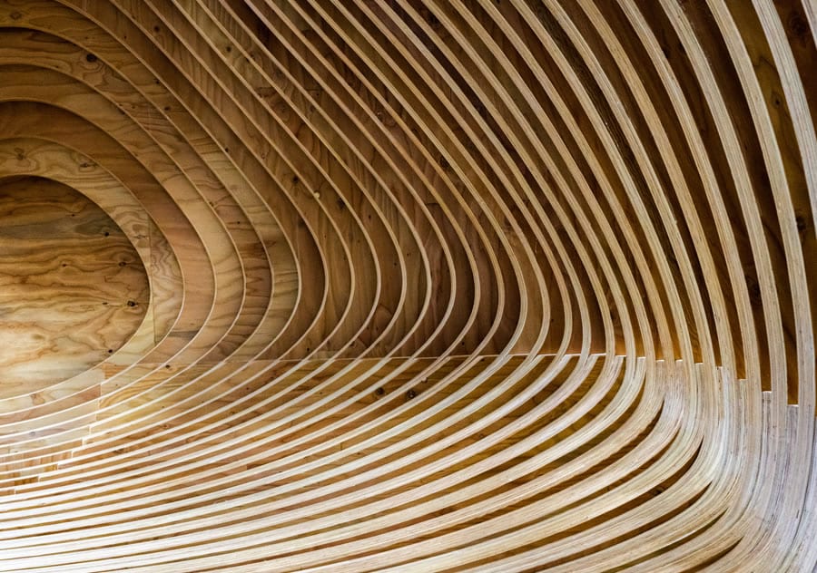 Curved wooden panels form an abstract, wave-like architectural design on a ceiling.
