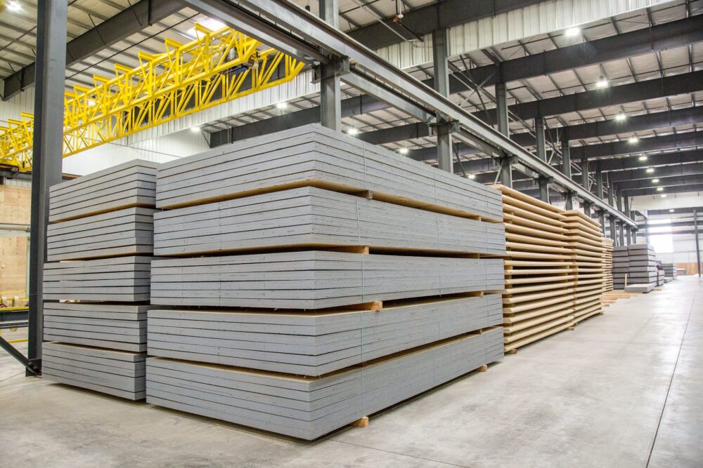 Stacks of flat, rectangular boards are neatly arranged inside a large, modern industrial warehouse.
