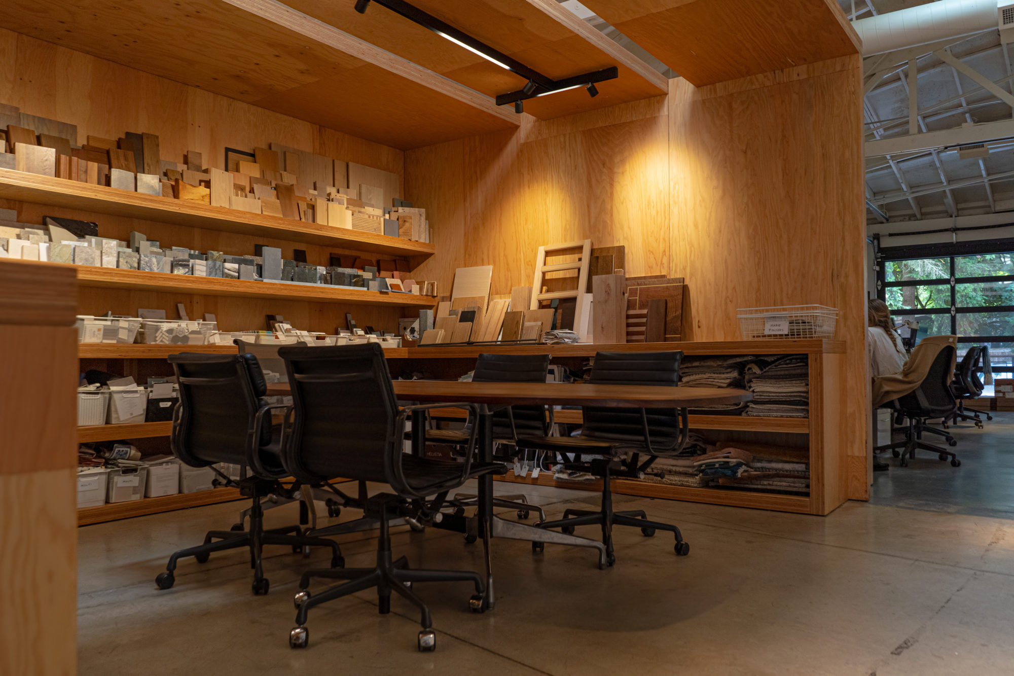 A modern meeting room with black chairs, wooden shelves, and sample materials displayed on the walls.
