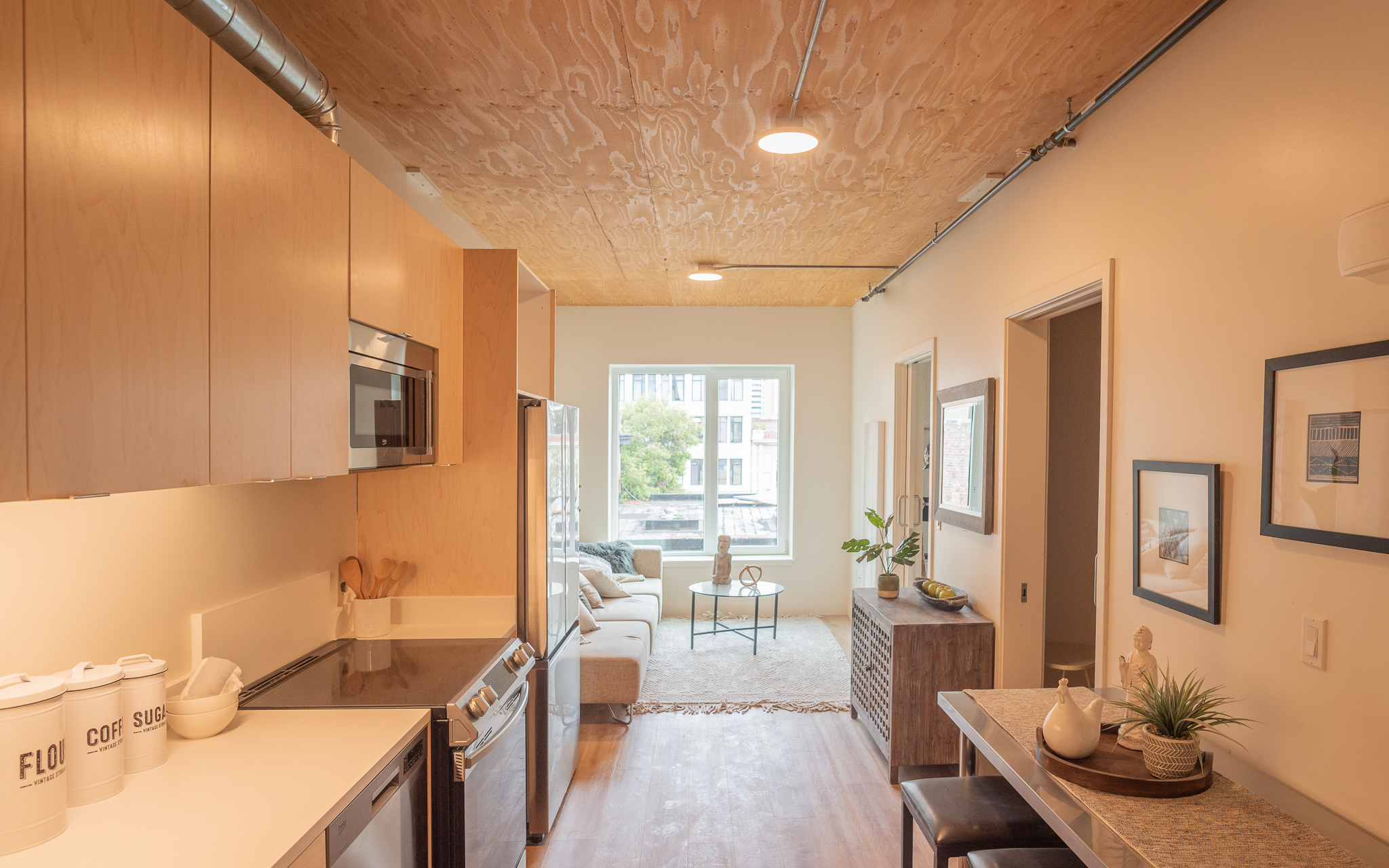 Modern studio apartment with a small kitchen, cozy living area, and large window letting in natural light.
