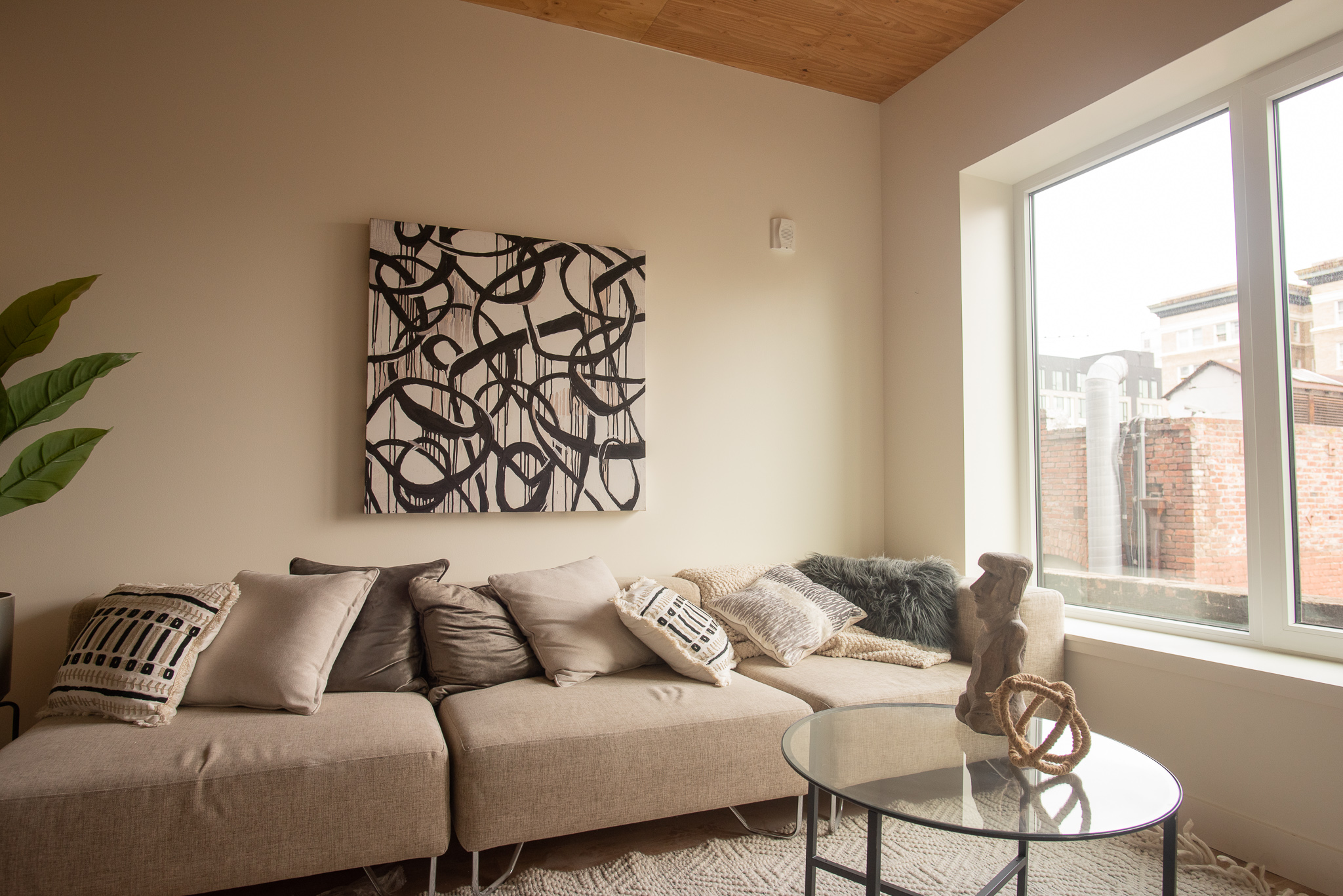 Modern living room with beige sofa, abstract wall art, large window, and decorative pillows and accents.