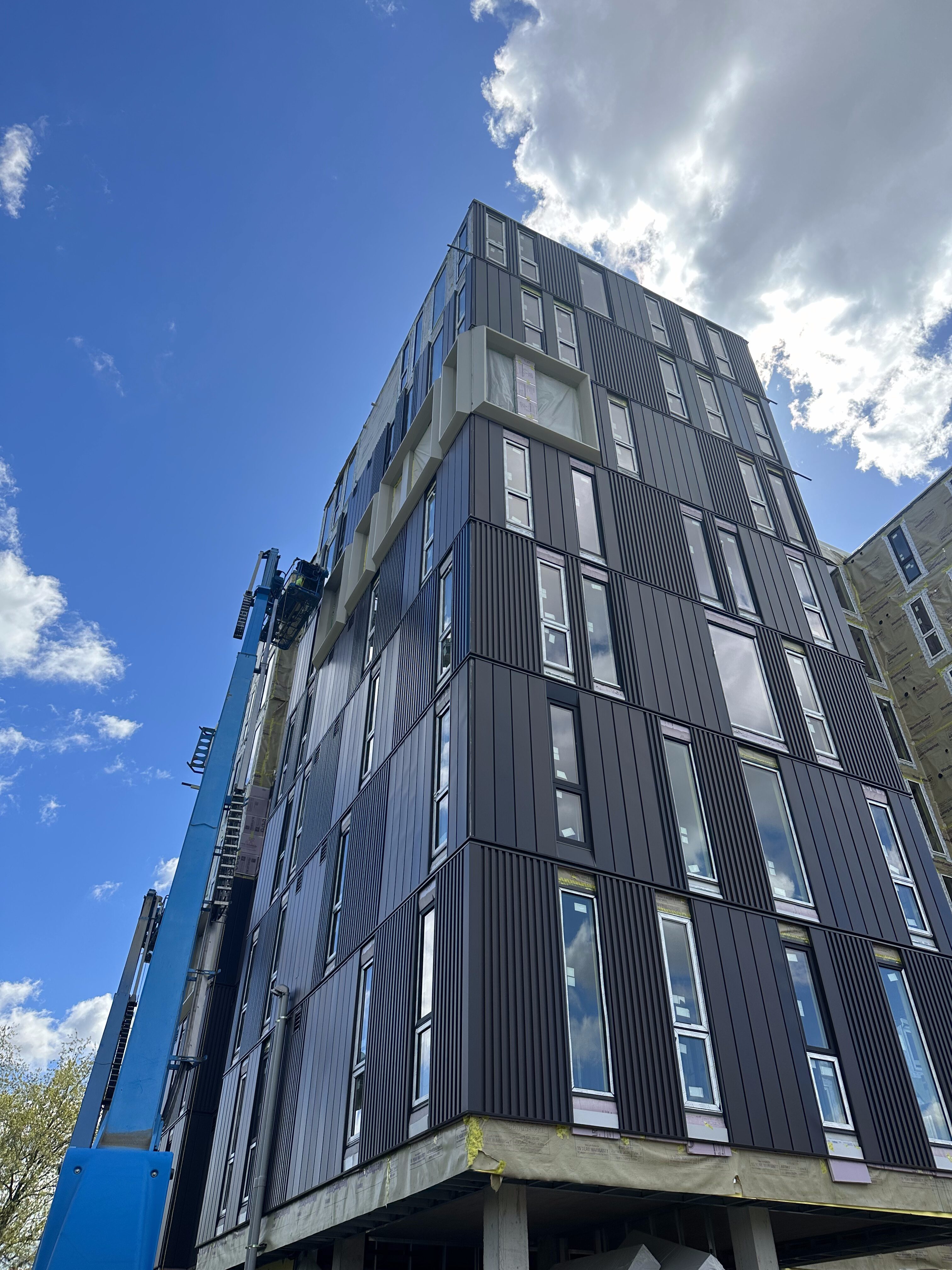 A modern black building under construction with a blue crane against a partly cloudy sky.